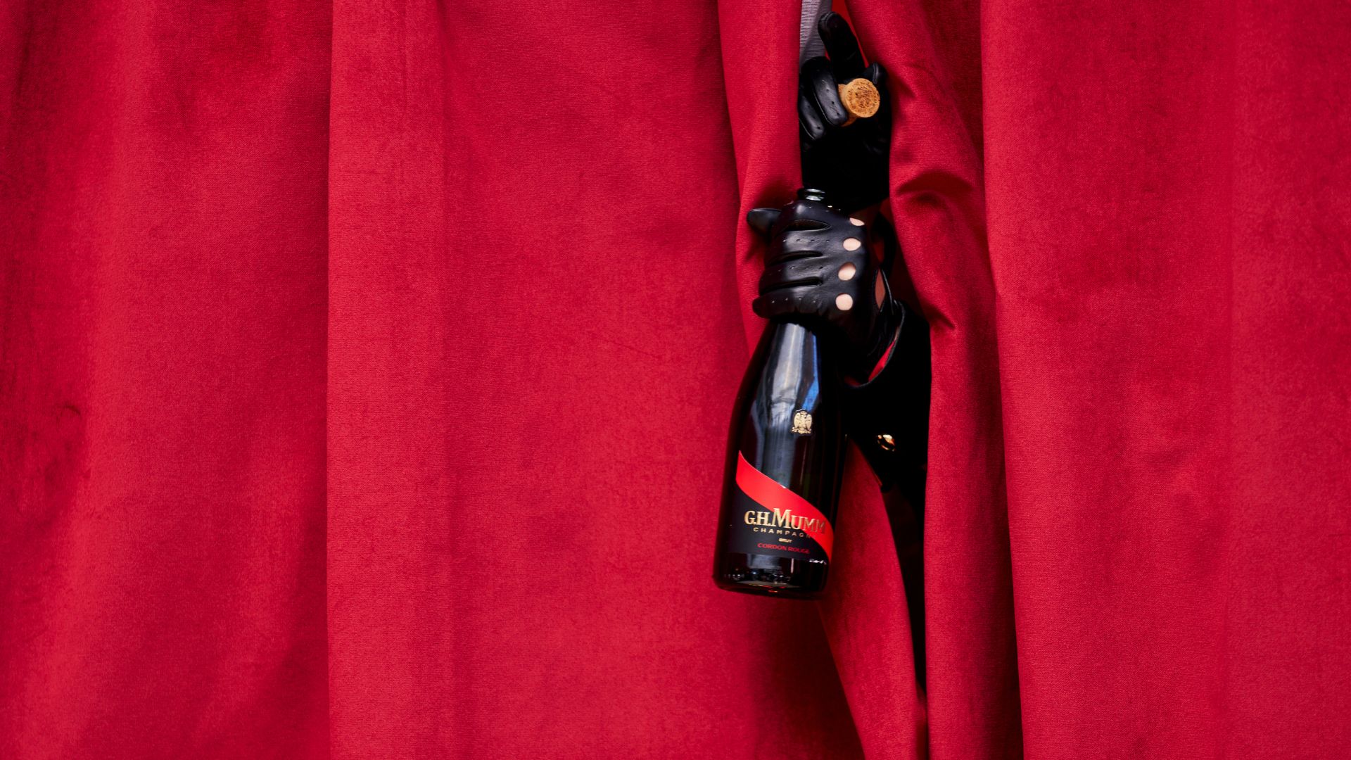 mumm corgon rouge held by a hand with a leather glove sticking out from a red curtain