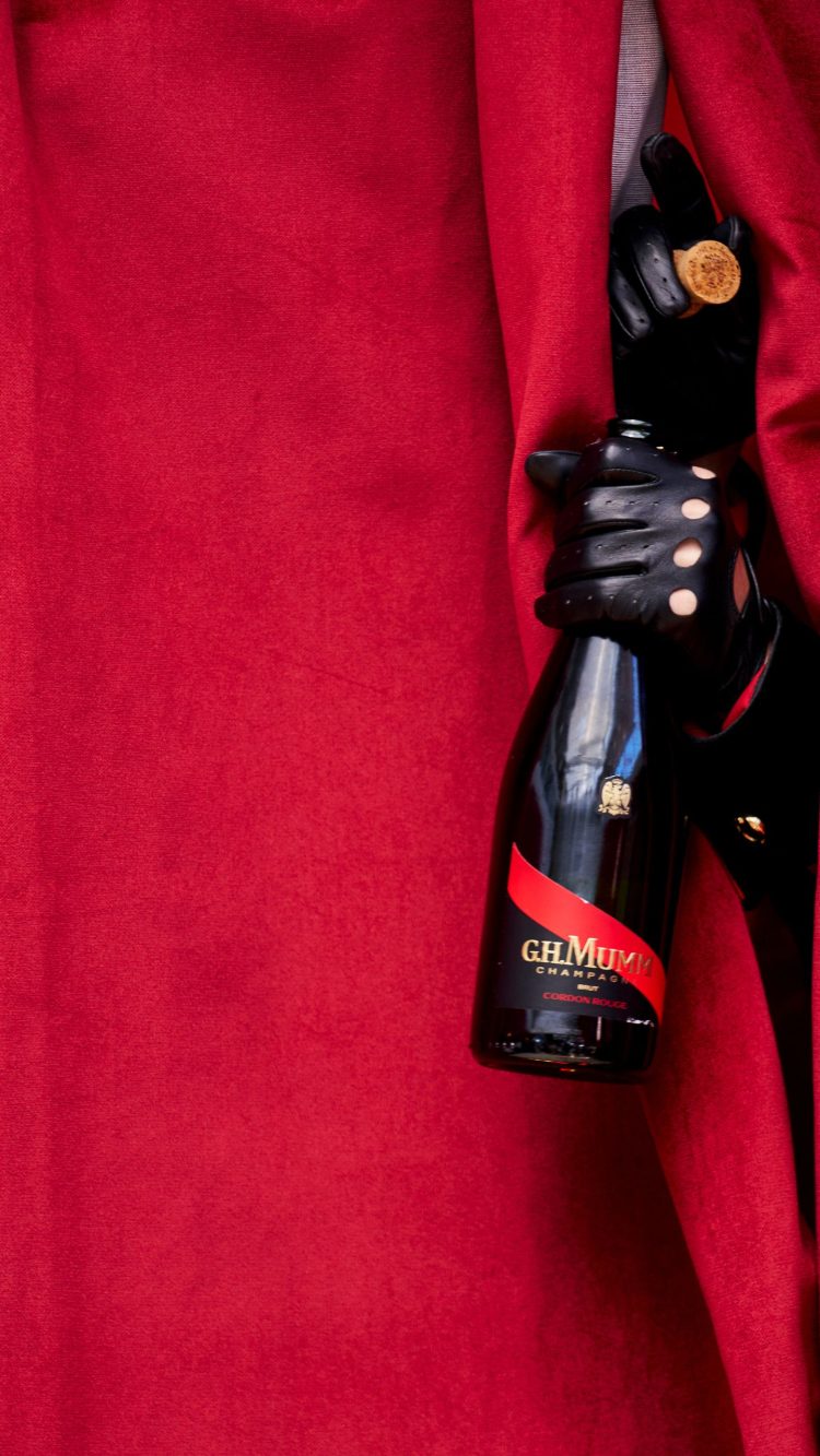 mumm corgon rouge held by a hand with a leather glove sticking out from a red curtain